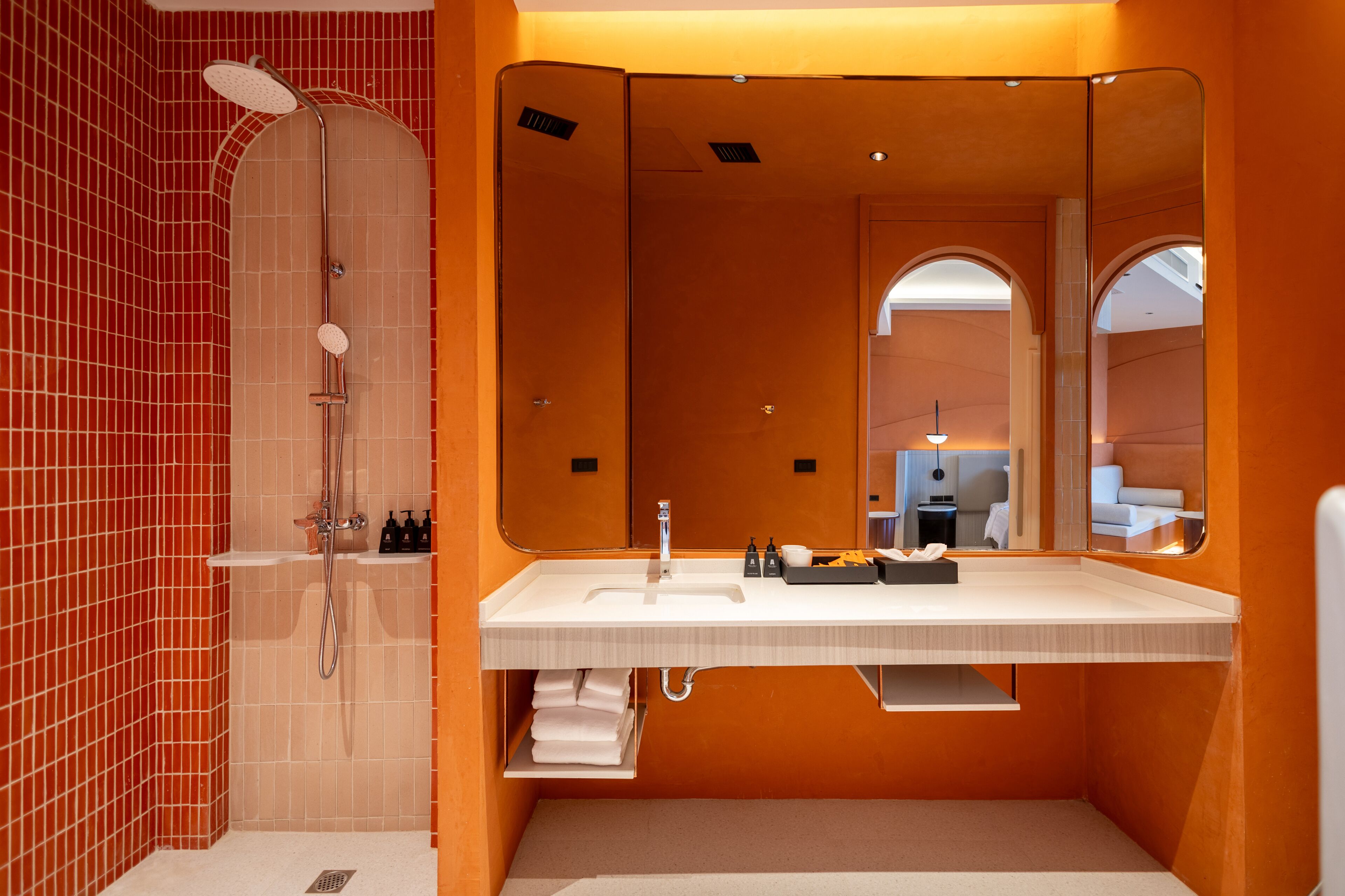 A modern bathroom with a large mirror, a shower, and a sink with toiletries.