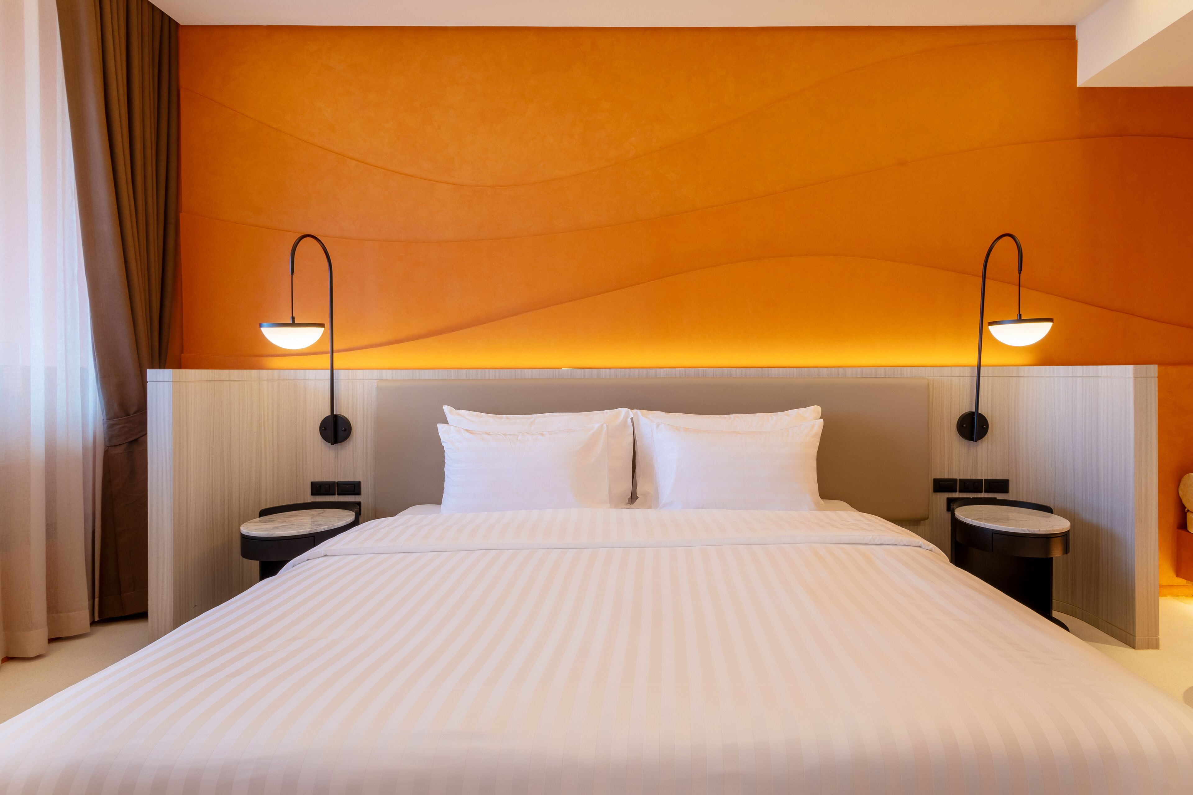 A hotel room with a large bed, two bedside tables, a headboard, and wall-mounted lamps.