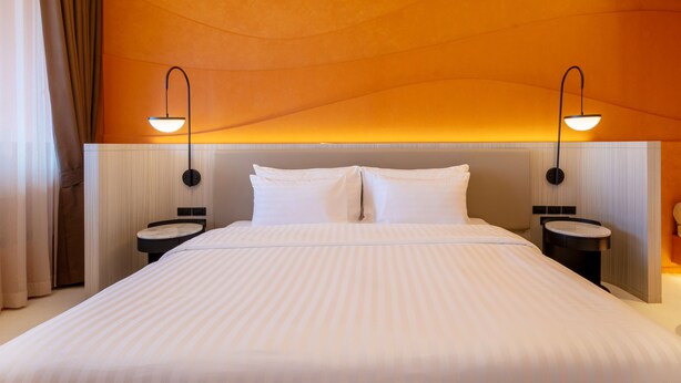Habitación de hotel con una cama grande, dos mesitas de noche, un cabecero y lámparas fijadas a la pared.
