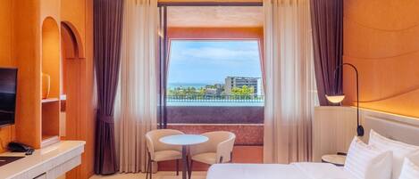 Une chambre d’hôtel équipée d’un lit, d’un bureau, d’une chaise, d’une petite table, d’une télévision et d’une grande fenêtre donnant sur la ville.