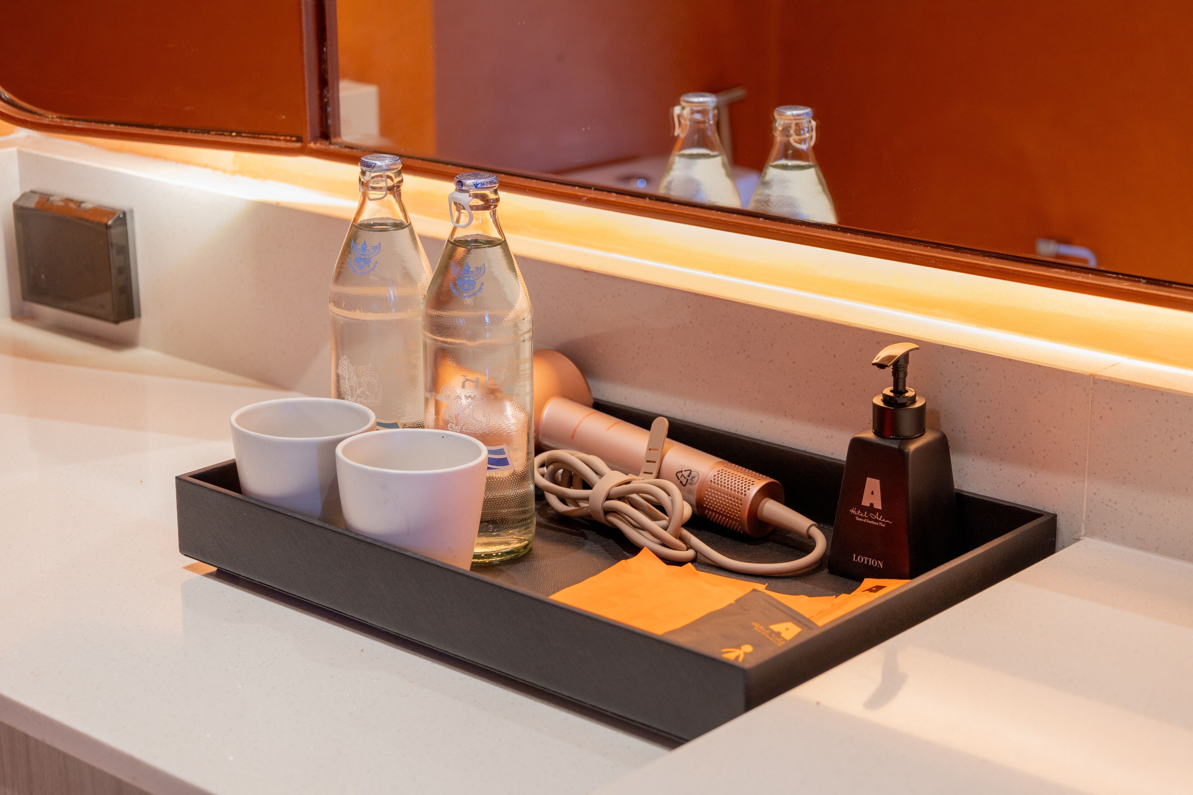 A hotel minibar with bottles, cups, and a hairdryer.