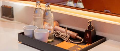 A hotel minibar with bottles, cups, and a hairdryer.