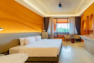 Habitación de hotel con una cama grande, un escritorio, dos sillas y vistas a zonas verdes por la ventana.