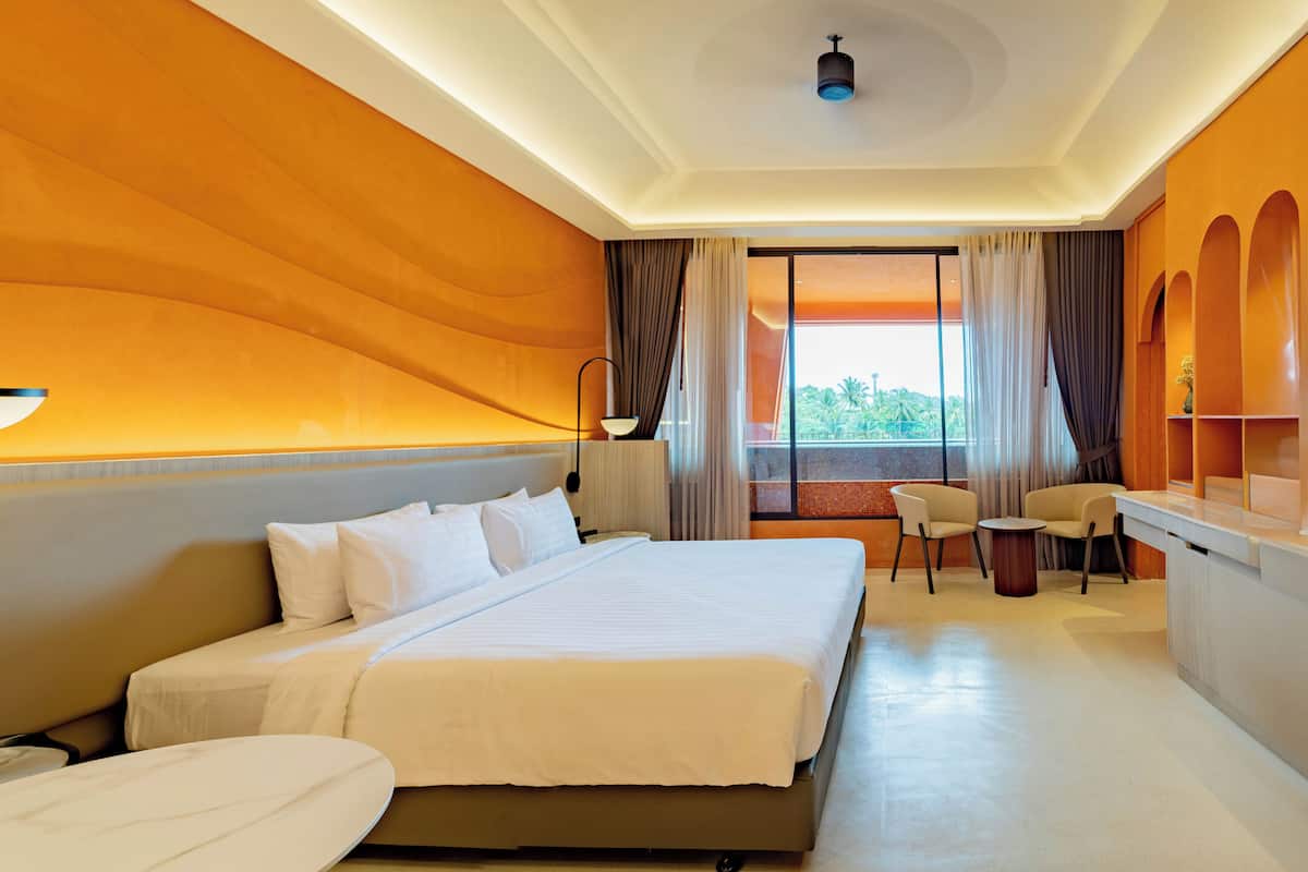 Habitación de hotel con una cama grande, un escritorio, dos sillas y vistas al exterior.