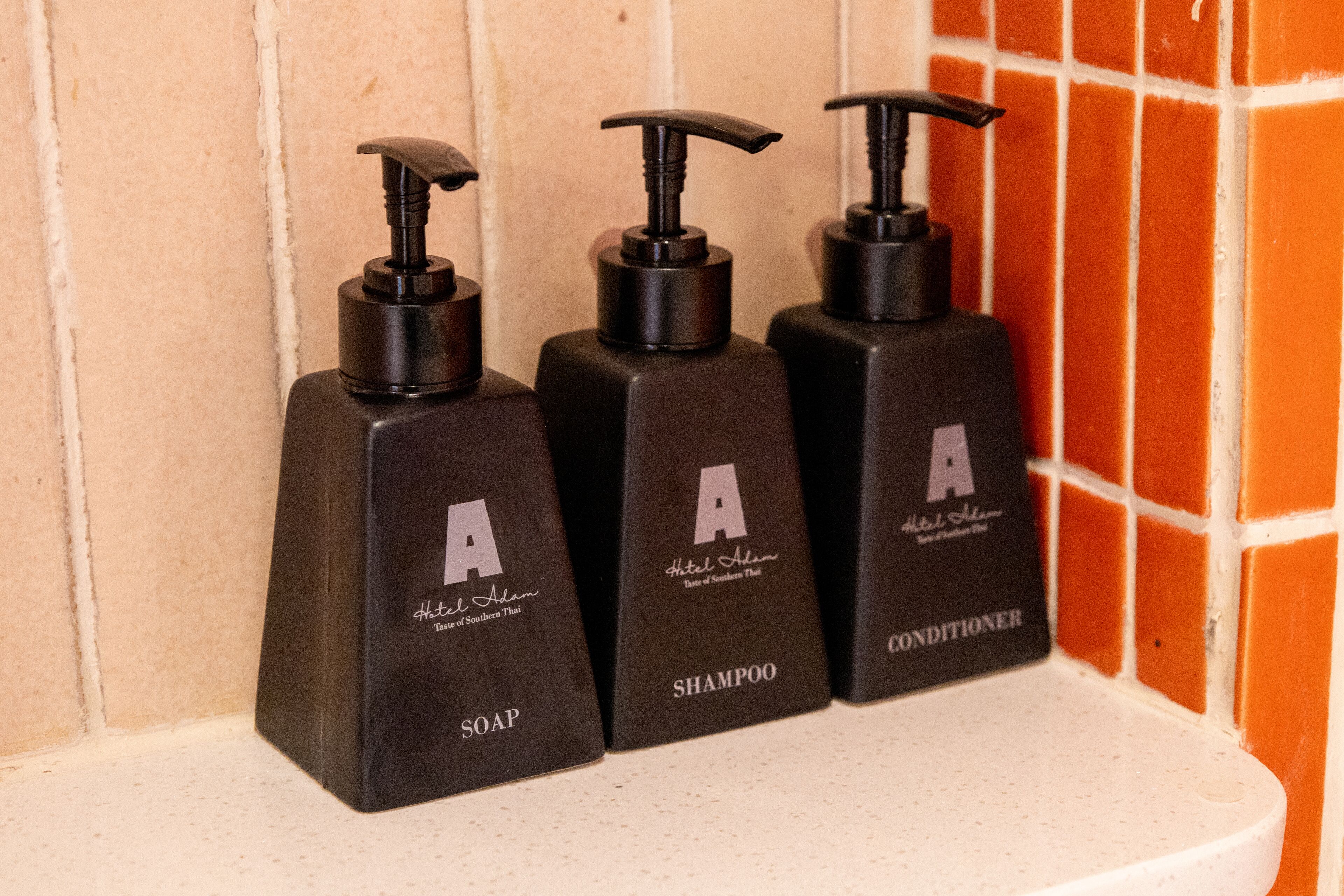 Three black bottles of Hotel Alam toiletries on a white shelf.