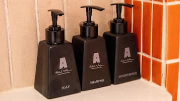 Three black bottles of Hotel Alam toiletries on a white shelf.