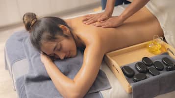 A person receiving a back massage on a massage table with a towel and a tray of massage stones.