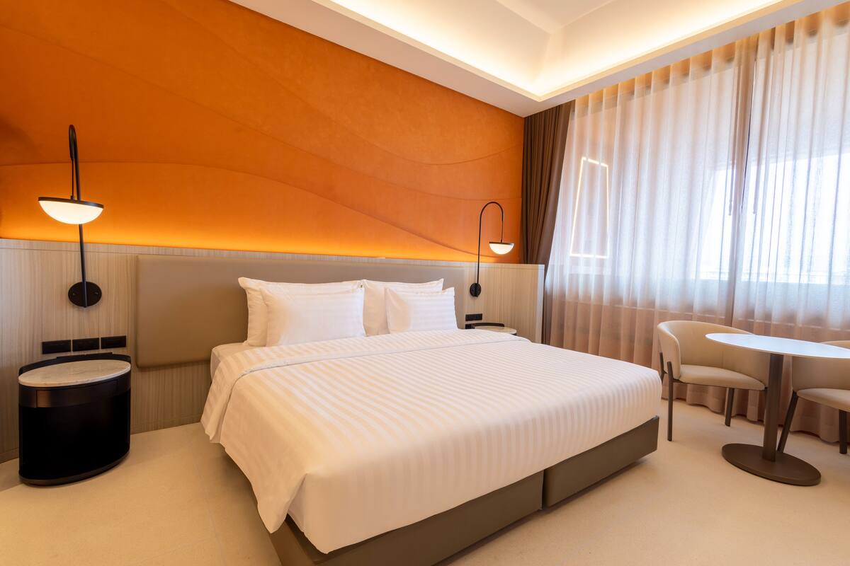Una habitación de hotel con una cama grande, dos mesitas de noche, una mesa redonda y una silla.
