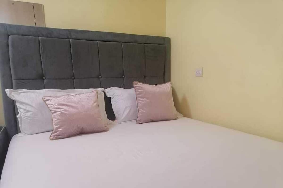 A bed with a grey upholstered headboard, two white pillows, and a light-colored bedspread.
