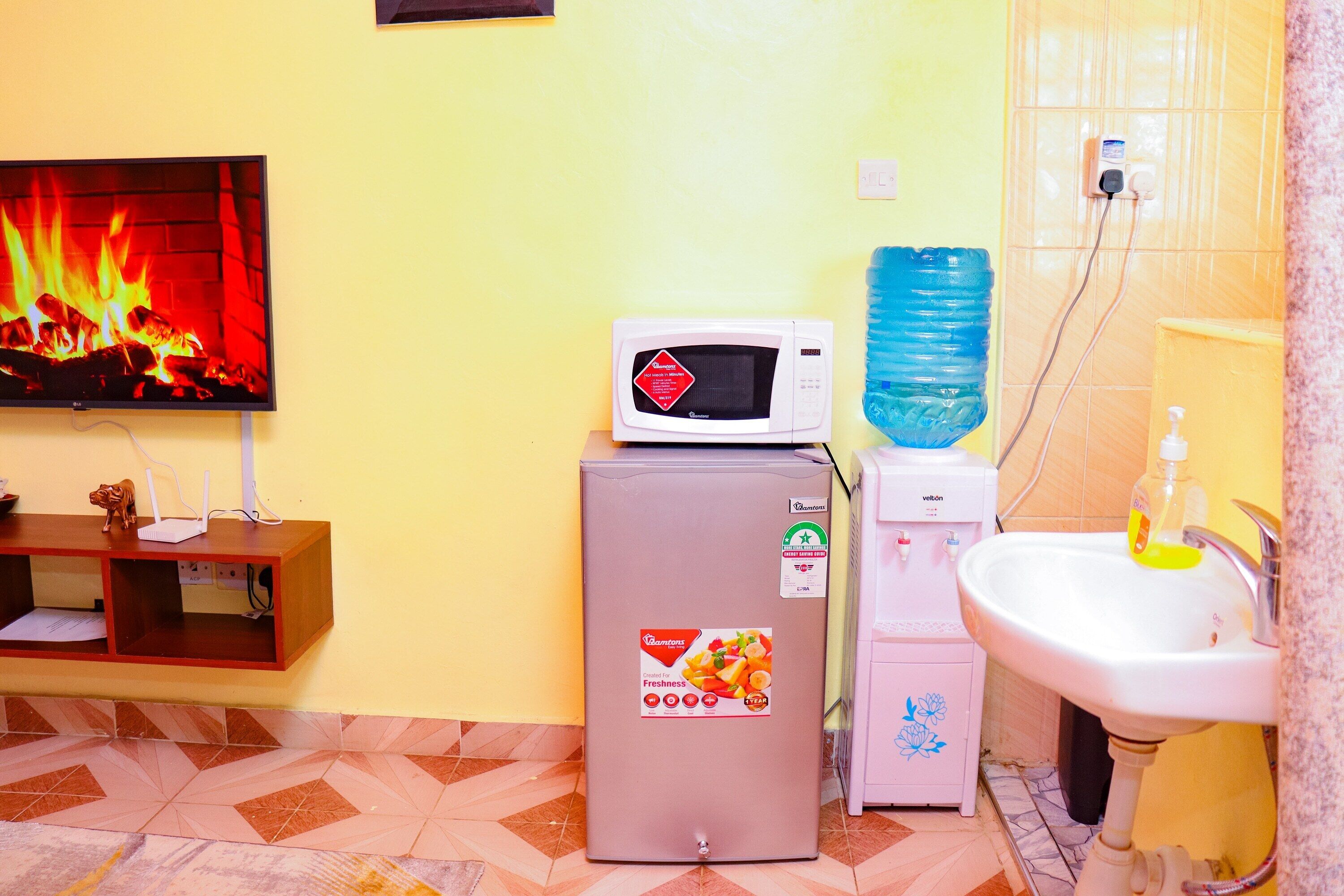 A compact living space with a television displaying a fire, a refrigerator, a water dispenser, and a sink.