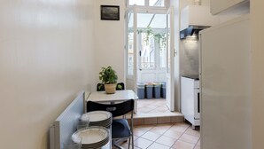 Une cuisine compacte avec un coin repas, des murs blancs, un sol carrelé et une fenêtre donnant sur l’extérieur.