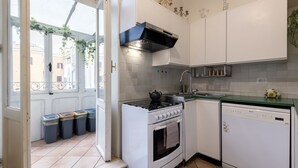 Une cuisine compacte équipée d’une cuisinière, d’un four, d’un lave-vaisselle et d’une fenêtre donnant sur des immeubles.