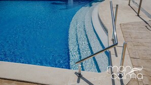 A swimming pool with clear blue water, a metal handrail, and a tiled walkway.