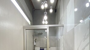 Un baño moderno con ducha de vidrio, paredes de azulejos blancos y un inodoro a la vista.
