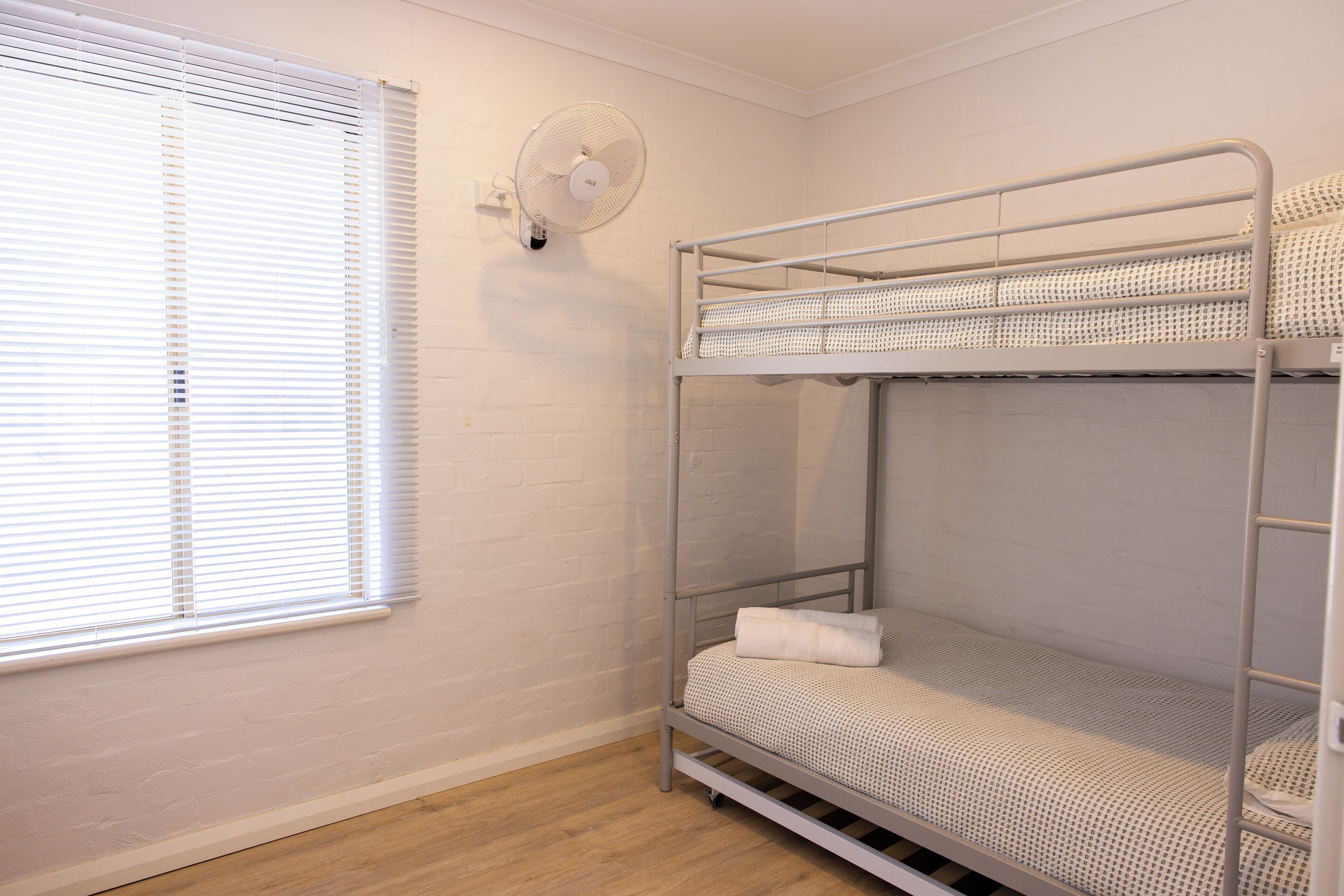Dormitorio con literas, ventana y ventilador de pared.