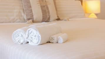 Una cama bien hecha con toallas blancas enrolladas y almohadas a rayas.