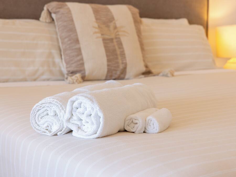 A neatly made bed with rolled white towels and striped pillows.