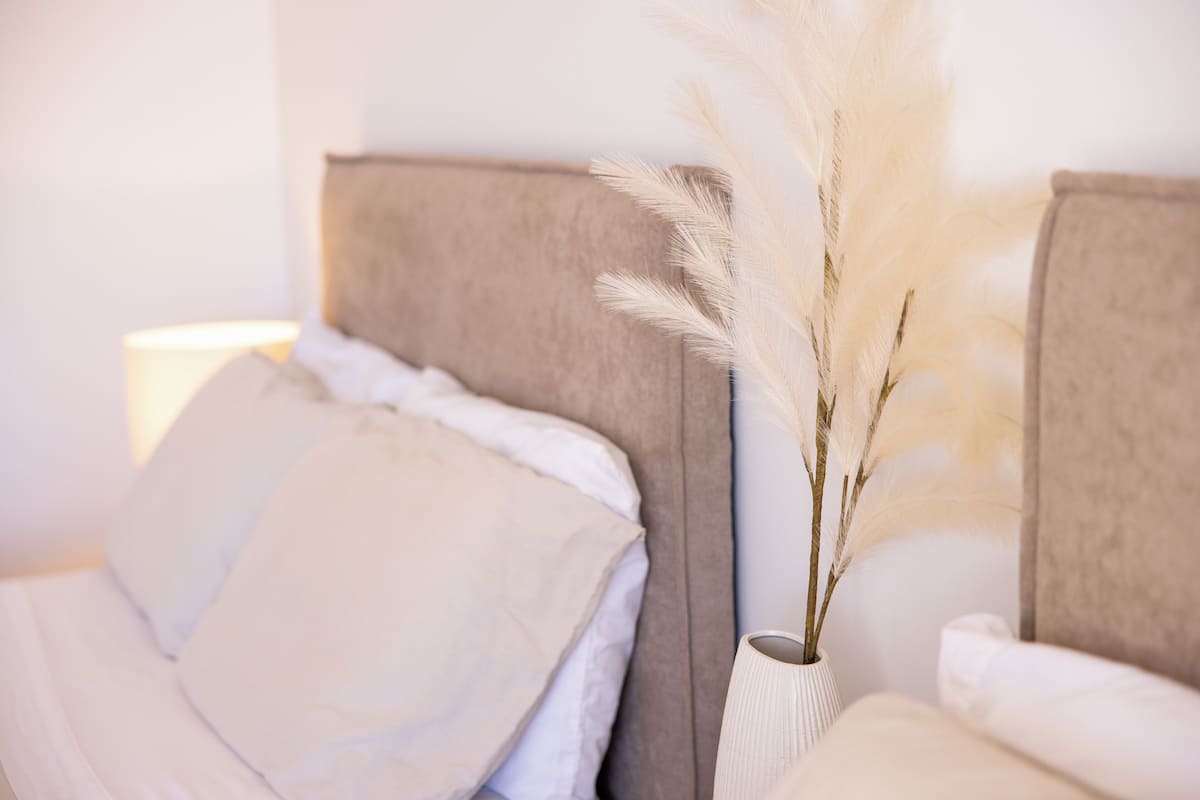 Un lit bien fait, avec du linge de lit blanc et un vase décoré de plumes blanches.