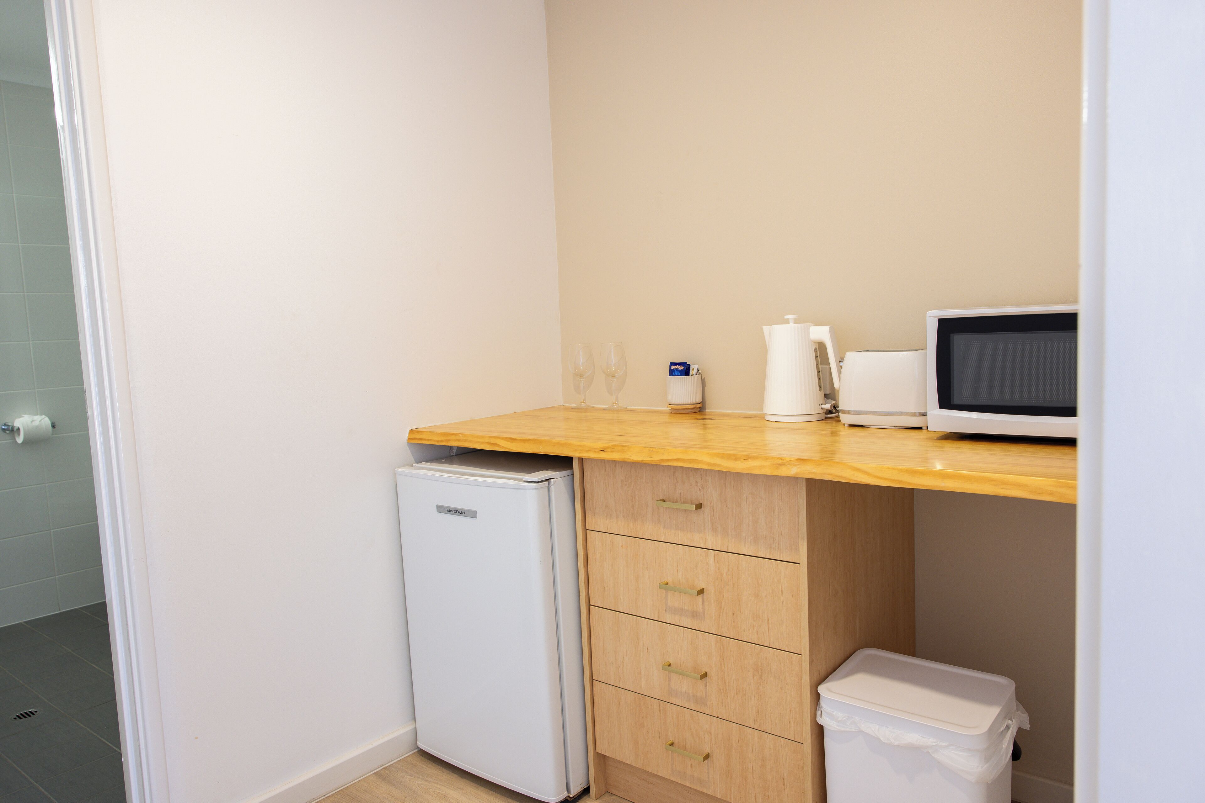 A compact kitchenette with a microwave, a small refrigerator, and a trash bin.
