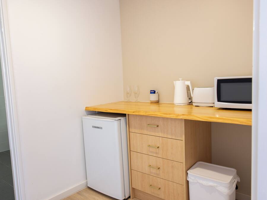 A compact kitchenette with a microwave, a small refrigerator, and a trash bin.