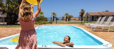 A swimming pool with a person standing in the water and another holding a yellow ball.