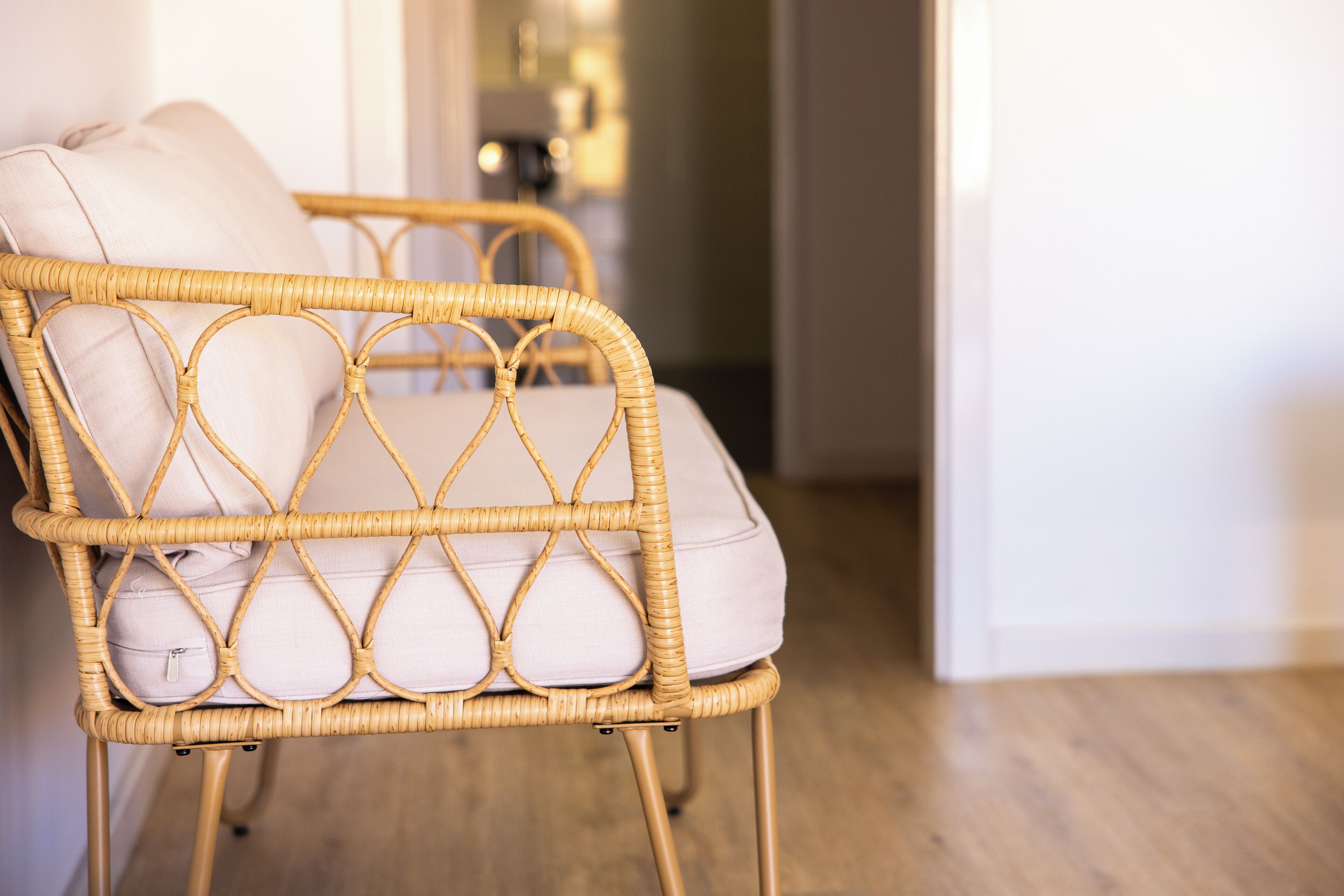 A wicker chair with a cushion, positioned in a room with wooden flooring and a white wall.