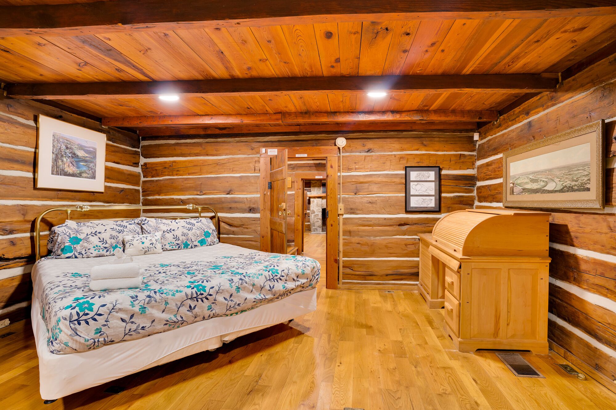Quarto de cabana de toras com cama, cómoda de madeira e quadros nas paredes.