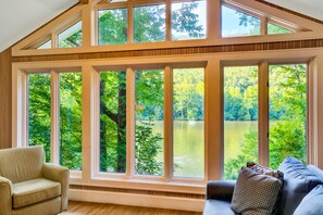 A room with large windows overlooking a lake, a sofa, and a chair.