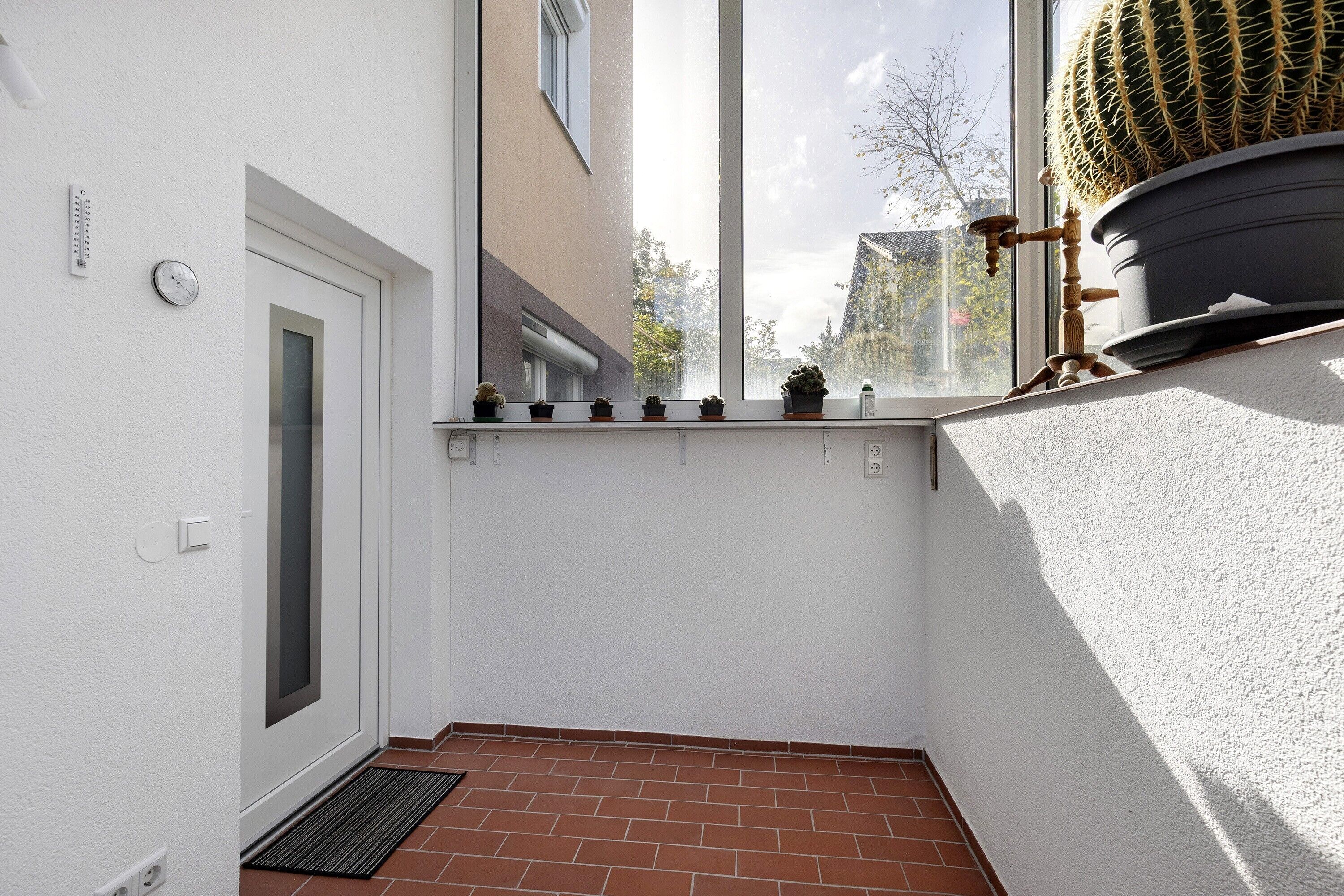 Un couloir étroit avec une fenêtre, une porte et une petite plante en pot posée sur le rebord de la fenêtre.