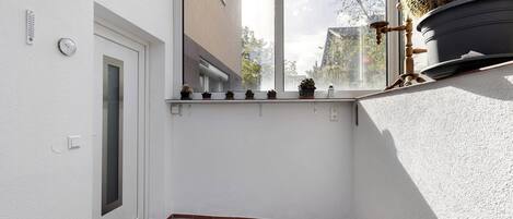 Un couloir étroit avec une fenêtre, une porte et une petite plante en pot posée sur le rebord de la fenêtre.
