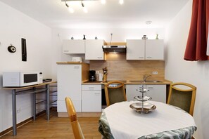 Cocina compacta con microondas, cafetera y lavaplatos. Hay una mesa de comedor con sillas y una bandeja de tres niveles sobre ella.