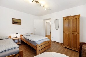 Une chambre avec deux lits simples, une armoire en bois, un bureau avec une lampe et un tableau au mur.