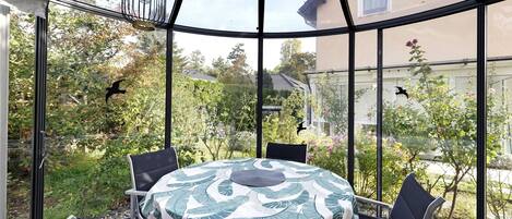 A conservatory with a round table, chairs, and a birdcage.