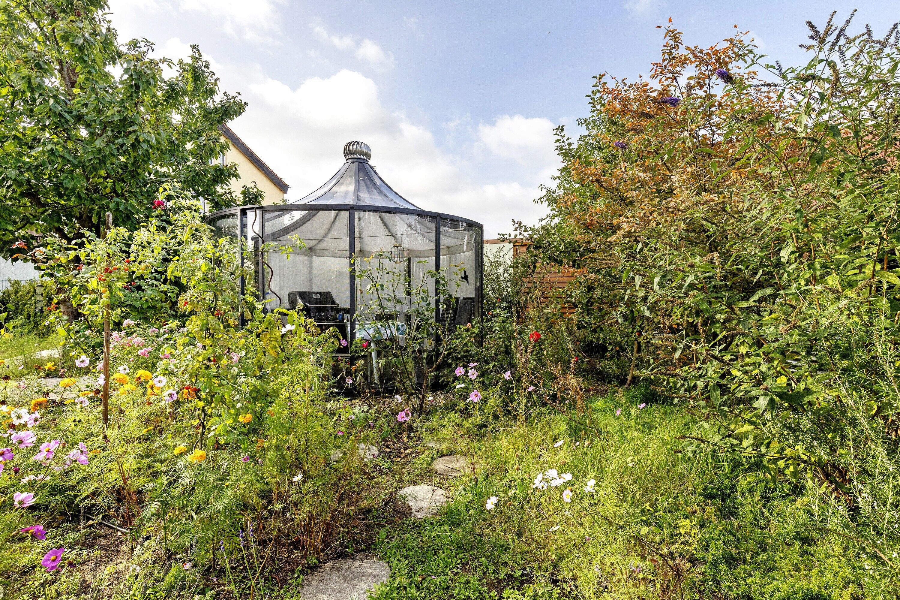 A garden with a glass greenhouse structure surrounded by various plants and flowers.