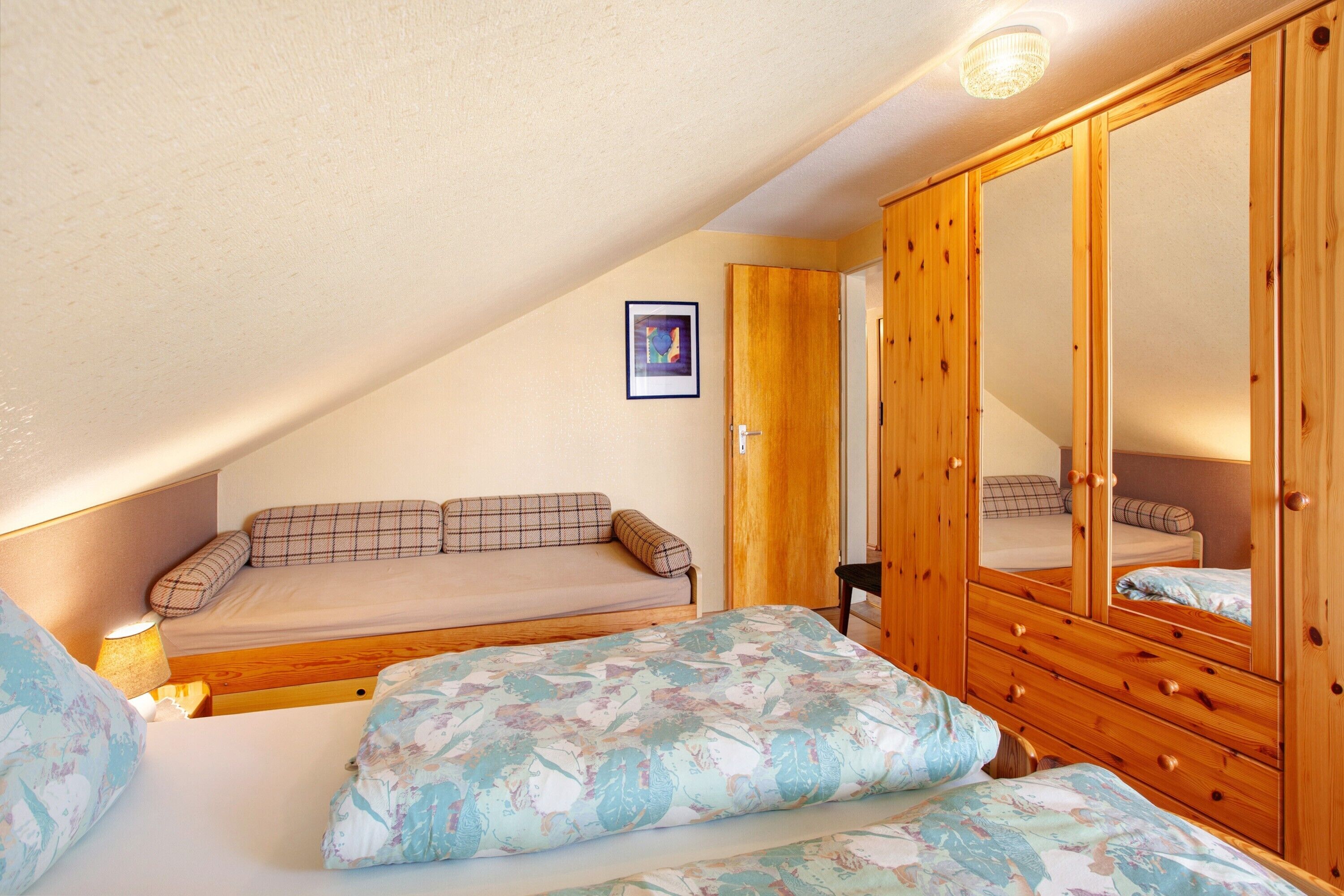 A bedroom with a bunk bed, a wooden wardrobe, and a framed picture on the wall.