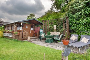 Une cabane rustique en rondins de bois, dotée d’une véranda, de meubles de jardin et d’un jardin.