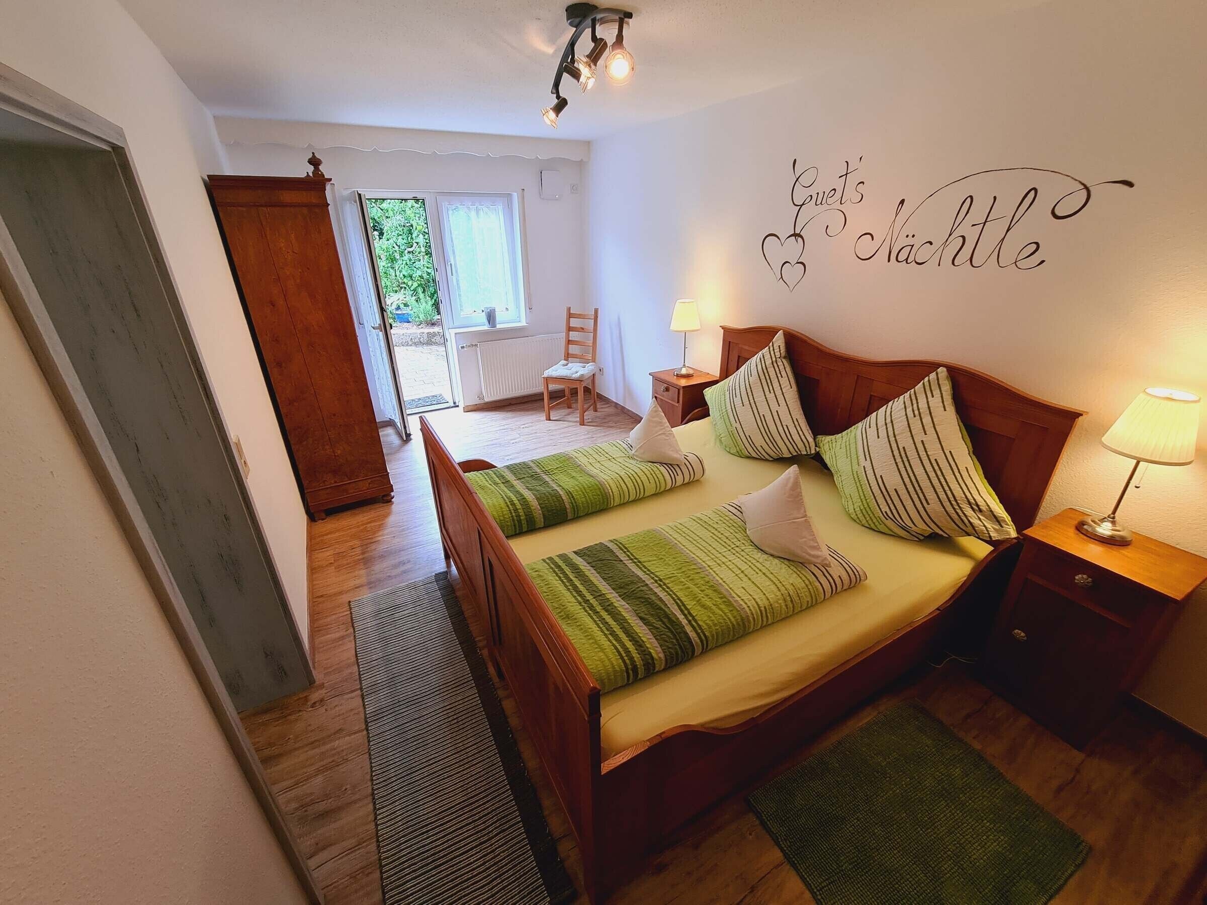 Un dormitorio con cama, mesitas de noche, una silla, un ventanal y un adorno en la pared.