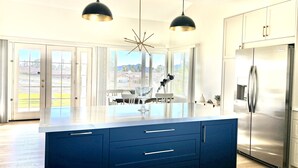 A modern kitchen with a central island, stainless steel appliances, and a large window offering a view of the outdoors.