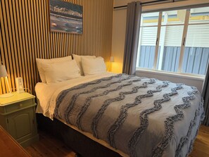 A neatly made bed with a grey and white patterned blanket, a bedside table with a lamp, and a wall-mounted picture.