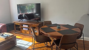 A living room with a TV, wooden entertainment unit, and a dining table with chairs.