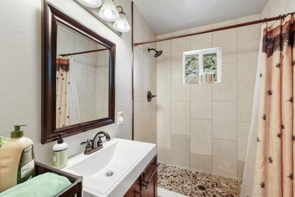 A bathroom with a large mirror, a sink, a shower with a glass door, and a window.