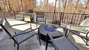 Eine Terrasse im Freien mit einem runden Tisch, Stühlen, einer Feuerstelle und einem Grill.