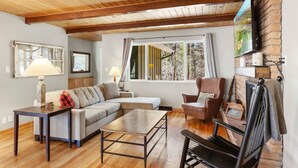 Ein gemütliches Wohnzimmer mit Holzbalkendecke, einer Couch, einem Couchtisch, einem Fernseher und einem Kamin.