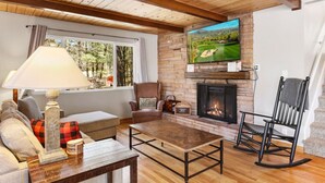 Ein gemütliches Wohnzimmer mit Kamin, einem an der Wand befestigten Fernseher und einer bequemen Sitzecke mit Sofa und Sesseln.