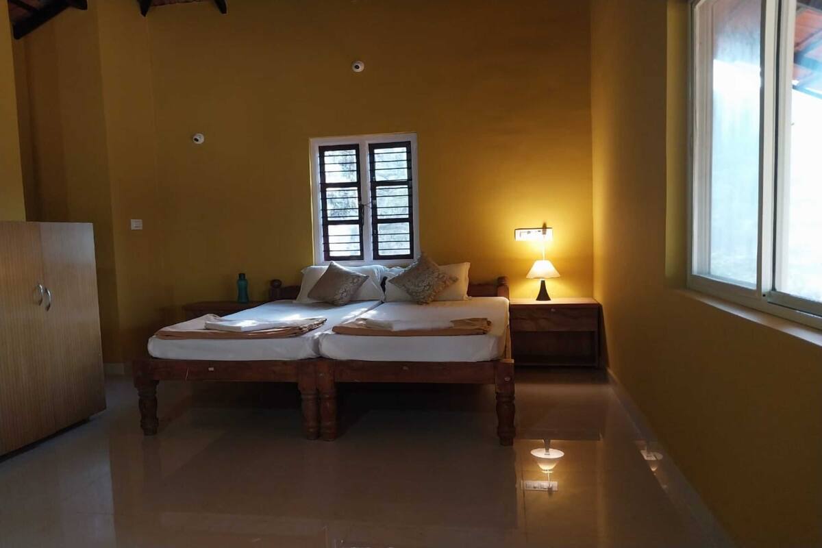 A bedroom with a double bed, a nightstand with a lamp, a window with blinds, and a wardrobe.