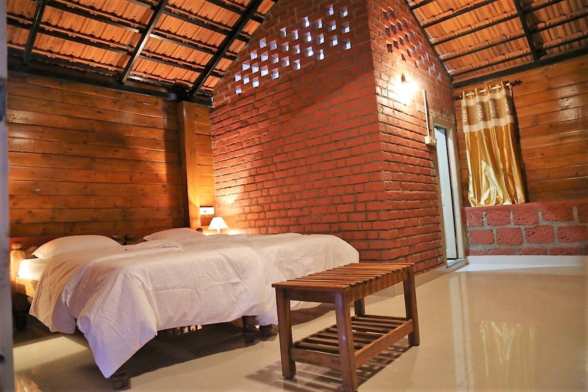 A room with two beds, a wooden bench, a brick wall, and a ceiling with a wooden beam structure.