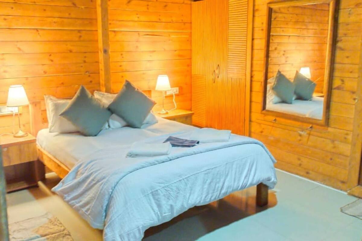 A wooden cabin-style bedroom with a bed, two bedside lamps, and a mirror on the wall.