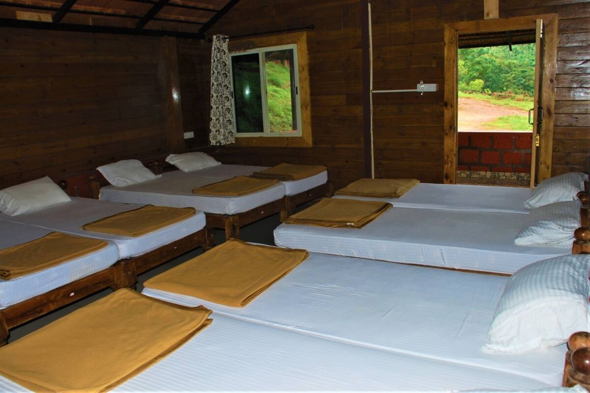 A cabin with four single beds, each with a pillow and a brown blanket. There is a window with a curtain, and a door leading outside.