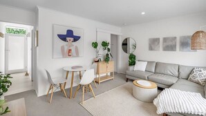 Een moderne woonkamer met een grijze bank, een ronde salontafel en een eethoek met witte stoelen.
