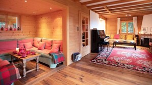 A cozy log cabin interior with a sofa, a piano, and a fireplace. - Chalet Le Haut Pré by Interhome (Villars)